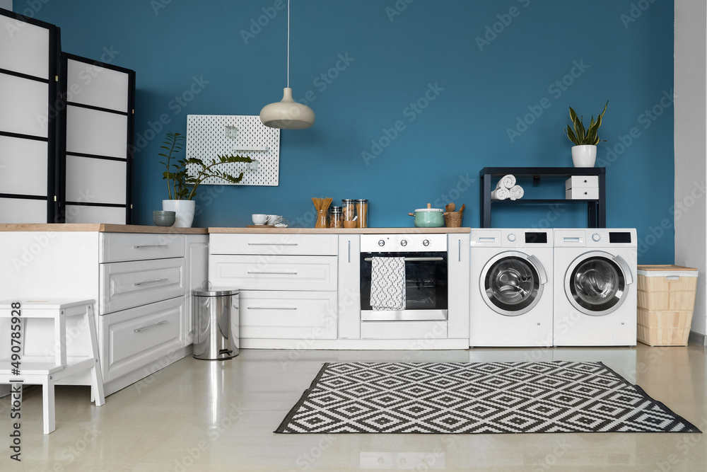 Interior of stylish kitchen with modern washing machines, oven and white counters