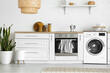 Interior of light kitchen with washing machine, oven and white counter