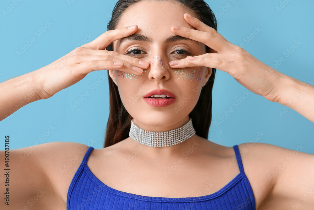 Woman with creative makeup touching face on blue background