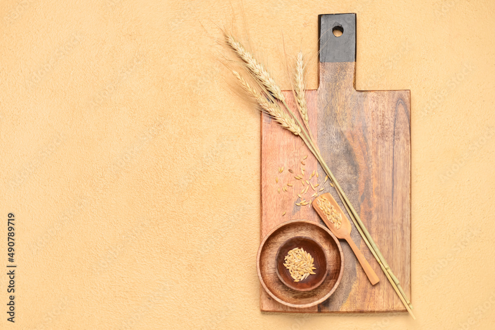 Wooden cutting board, bowls and wheat spikelets on beige background