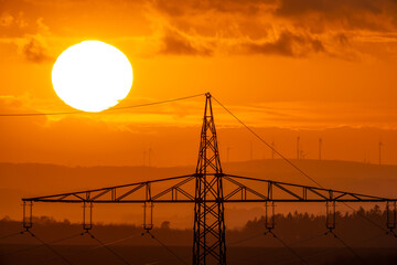 Canvas Print - View of a transmission tower against the orange sun setting down