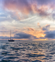 Poster - Vertical scenic shot of the sea and a boat during sunset under the sky and beautiful clouds