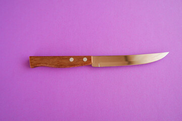 Sticker - Closeup shot of a shiny sharp knife with a brown wooden handle over the purple surface