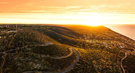 Wall Mural - Aerial view of winding roads on a hill near the shore on the sunset