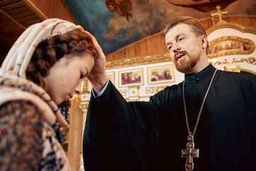 Wall Mural - a priest blesses a teenage girl in a headscarf in an Orthodox church after a festive church mass