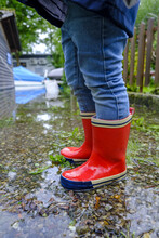 Vertical Shot Of A Kid's Legs Wearing Blue Jeans And Galoshes On A Rainy Day Standing Outside