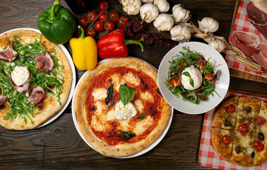 Wall Mural - Top view of different pizzas, a salad, and vegetables on a wooden table