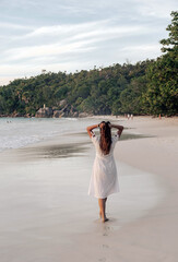 Canvas Print - Vertical view of the Caucasian female walking on the sandy beach with white dress in Seychelles