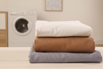 Poster - Stack of clean bed linens on white wooden table in laundry room