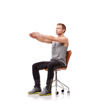 Keeping His Limbs Long And Lean. A Handsome Young Man Wearing Gym Clothes And Stretching While Seated In An Office Chair Against A White Background.