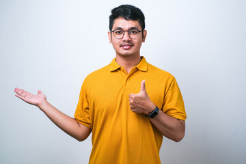 Wall Mural - Asian man wearing casual shirt showing palm hand and doing ok gesture with thumbs up, smiling happy and cheerful