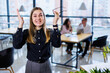 © DSMT - A young woman in a black shirt with bright emotions on her face, she stands against the background of her colleagues and gesticulates with her hands