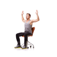 Stretching Out His Chest. A Handsome Young Man Wearing Gym Clothes And Stretching While Seated In An Office Chair Against A White Background.
