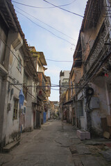 Poster - Vertical shot of an empty street between old rustic abandoned houses covered with moss