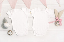 Two White Baby Bodysuit Mockup With Easter Decor On White Wood Background. Easter Eggs And Gnome With Rabbit Ears