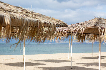 exotic beach on the beach with parasol. A lonely empty beach umbrella made of reeds. Beautiful dry branches of palm trees on the roof against the backdrop of the beach.