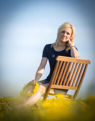 Sticker - Vertical shot of the Caucasian female sitting on the wooden chair in the yellow dandelion field