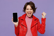 Young overjoyed happy woman 20s wear red leather jacket hold in hand use mobile cell phone with blank screen workspace area do winner gesture isolated on plain pastel light purple background studio