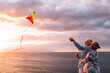 © Daniel - Cheerful senior couple having fun flying kite in front of beautiful seascape against cloudy sky. Active old man and woman with kite in midair at beach. Elderly partners enjoying in front of sea