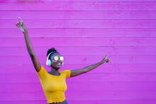 African Girl Dancing Alone, With Headphones On Her Ears, Listen To Music In A Silent Disc, Sense Of Freedom And Joy, Contrast Of Yellow Shirt And Pink Color Background
