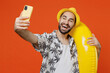 © ViDi Studio - Young smiling tourist man wear beach shirt hat hold inflatable ring doing selfie shot on mobile cell phone isolated on plain orange background studio portrait Summer vacation sea rest sun tan concept