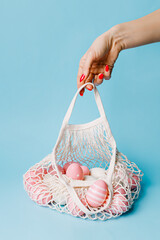 Wall Mural - Woman's hand holding crochet bag full of colorful eggs against pastel blue background. Minimal Easter holiday concept. Spring holiday shopping, advertisement or sale banner idea.