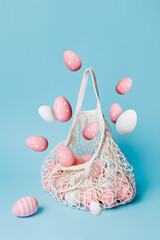 Wall Mural - Crochet shopping bag full of colorful eggs flying in the air against pastel blue background. Minimal Easter holiday concept. Spring holiday shopping, advertisement or sale banner idea.