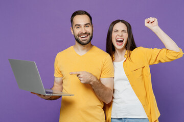 Young fun freelancer caucasian couple two friends family man woman together in yellow clothes hold use work on laptop pc computer do winner gesture isolated on plain violet background studio portrait