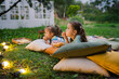 © tgordievskaya - Family summer outdoor movie night. Girls lying on blanket and pillows, eating homemade popcorn and watching film on DIY screen with from projector. Summer outdoor weekend activities with kids.
