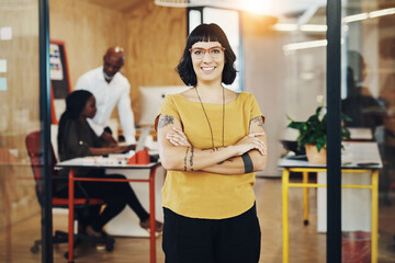 Sticker - Its a good feeling to succeed. Shot of a creative businesswoman standing in her office with colleagues blurred in the background.