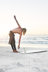 Canvas Print - Hes all set to conquer the ocean. Full length shot of a handsome young man stretching before going surfing at the beach.