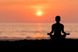 © Tarokmew - Silhouette of young female sitting practices yoga and meditating in lotus position alone on the rock in the morning at the sea with beautiful sunrise and orange sky. She felt calm and happy.