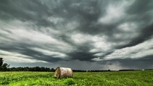 Time Lapse Shot Of Dark Grey Clouds Flying At Sky Over Agricultural Field With Hay Bale