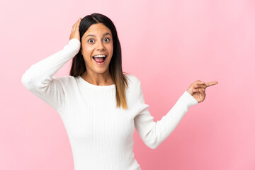 Poster - Caucasian girl isolated on pink background surprised and pointing finger to the side