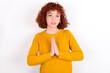 © Jihan - young redhead girl wearing yellow sweater over white background keeps palms pressed together in front of her having regretful look, asking for forgiveness. Forgive me please.