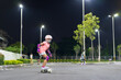 © kornnphoto - asian child or kid girl playing surf skate or skateboard in skating rink or sport public park at night to wearing face mask and helmet with elbow pads wrist and knee support for body safety to protect