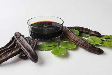 Wall Mural - carob molasses in glass bowl and in wooden spoon and carob pods on rustic background, locust bean healthy food, Ceratonia siliqua ( harnup )