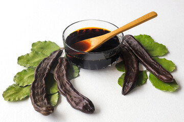 Wall Mural - carob molasses in glass bowl and in wooden spoon and carob pods on rustic background, locust bean healthy food, Ceratonia siliqua ( harnup )