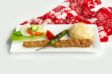 Turkish style adana kebab with rice and salad in a dish isolated on colorful table cloth side view on grey background