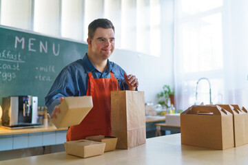 Wall Mural - Cheerful young Down Syndrome waiter working in take away restaurant, social inclusion concept.