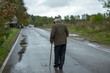 © Олег Копьёв - Old man walks down road. Pensioner with stick for support. Man with leg injury.