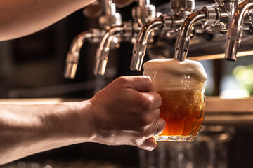 Wall Mural - Hand holding mug of beer filled from the tap with foam floating out of the glass