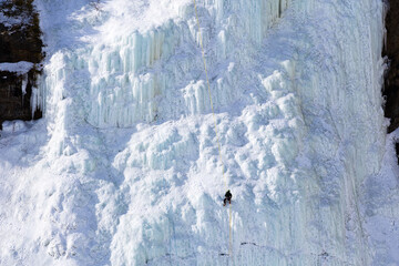 Wall Mural - Ice climber on steep frozen cliff seen during a beautiful sunny winter day in the Montmorency Falls Park, Quebec City, Quebec, Canada