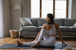 © fizkes - Young 30s woman practicing yoga asana sit on mat in living room, side view. Female in white sportswear perform Half Lord of the Fishes Pose, Ardha Matsyendrasana. Sport at home in quarantine concept