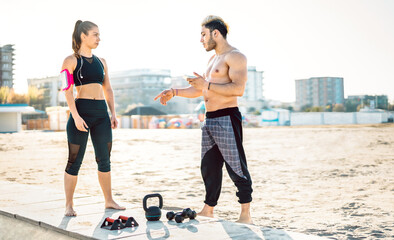 Male coach training athletic woman for calisthenic exercising at beach location - Alternative work out and body care concept in urban sport environment - Warm bright backlight filter