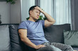 © Liubomir - Upset Asian man at home, tired and depressed sitting on the couch in the living room