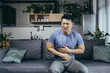 © Liubomir - Asian man himself at home sick sitting on the couch, has severe abdominal pain, man in the living room