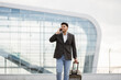 © sofiko14 - Portrait of young handsome Indian business man walking outside to station or airport talking on the phone and carrying suitcase.
