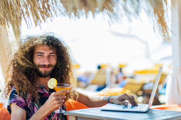 long curly haired man sitting in beach and working laptop vacation