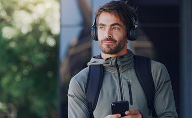 Poster - A good playlist is all you need. Shot of a man walking outside wearing headphones and using his cellphone.